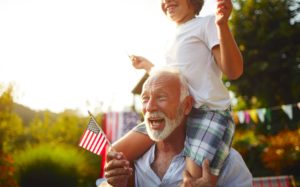Older man holding small American flag with child on his shoulders