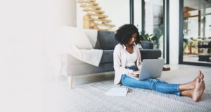 Smiling woman sitting on floor looking at laptop