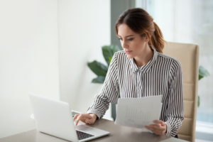 Woman looking at laptop holding documents