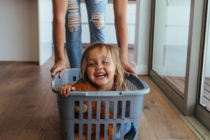 Child being pushed in a plastic laundry basket.