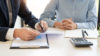 Two men sitting around table with clipboard and calculator