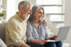 Old couple sitting on couch looking at laptop