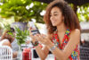 A young woman sits at an outdoor cafe making a purchase on her phone after learning how cash back works on credit cards.