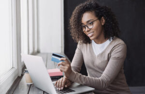 A woman smiles as she makes an online purchase after learning why it's often best to use a credit card over cash.