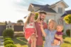 Young family holding two kids and showing keys to their new house.