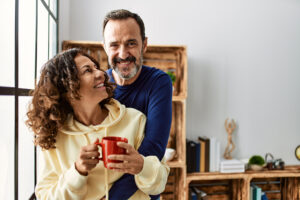 Middle age couple smiling, happy and drinking coffee, standing by a window.