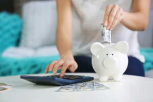 Female counting on a calculator and putting money into a piggy bank.