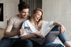 Happy couple sitting together holding a UCCU card looking at a laptop.