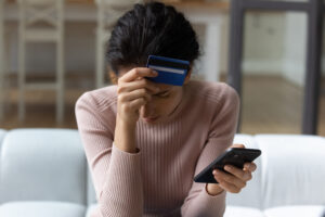 Distressed woman holding a credit card and smart phone.