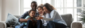 African American family with kids sitting on a couch in a living room using a smart phone.