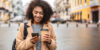 Young woman smiling at phone holding coffee