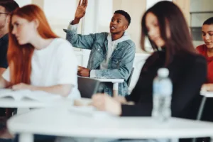 Boy sitting at a school desk raising his hand