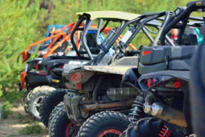 Multiple utv/atv lined up in a row outside in green forest.