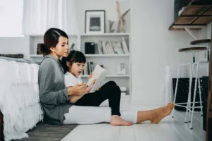 Young mom sitting on the floor reading with young daughter on her lap
