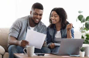 Couple smiling looking at documents, sitting on a couch with a laptop computer.