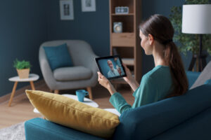 Young Woman sitting on a couch, using Telehealth with an iPad.