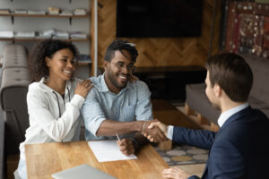 Couple smiling, sitting in a home shaking hands with a bank advisor.