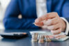 Person in a blue coat counting coins and paper money with a calculator.