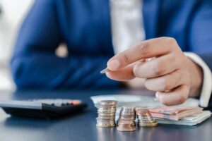 Person in a blue coat counting coins and paper money with a calculator.