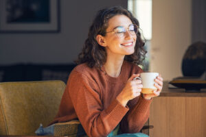 Woman smiling optimistically, holding a mug, sitting on a chair.