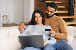 Man holding a bank card, woman smiling looking at a laptop.