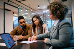 Man and woman signing a document, with a businesswoman pointing at the document.