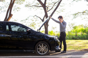 Man on the phone as he inspects his car engine, pulled over on the side of the road.