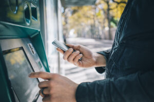 Person holding a phone while using an ATM.