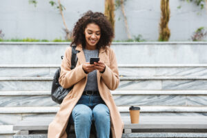 Woman sitting outside on a bench looking at a phone.